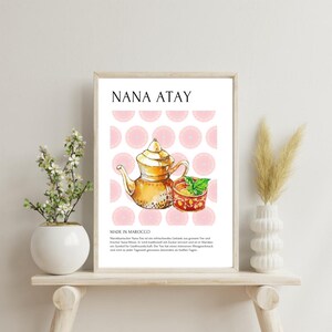 Könnte beinhalten: Ein weißes Poster mit dem Text "NANA ATAY" in schwarzer Schrift. Das Poster zeigt eine Aquarell-Illustration einer goldenen Teekanne und einer roten Teetasse mit Minzblättern. Der Hintergrund ist ein rosa-weißes Muster aus Kreisen. Der Text "MADE IN MOROCCO" befindet sich unter der Illustration, gefolgt von einer Beschreibung des Tees auf Deutsch.
