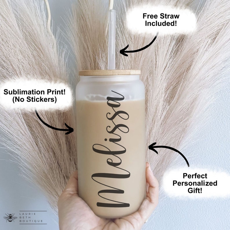 May include: A frosted glass tumbler with a bamboo lid and a straw. The tumbler is personalized with the name "Melissa" in black script. The tumbler is filled with a light brown liquid.