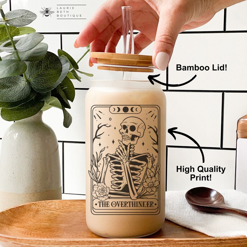 May include: A glass reusable water bottle with a bamboo lid and a black and white illustration of a skeleton with the text "The Overthinker".
