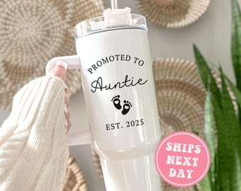 May include: White stainless steel tumbler with a black handle and a black design that says "Promoted to Auntie Est. 2025" with two black footprints.