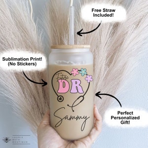 May include: A personalized tumbler with a brown background and a pink and blue heart with the text "Future DR" inside. The heart is surrounded by flowers. The name "Sammy" is written below the heart. The tumbler has a bamboo lid and comes with a free straw.