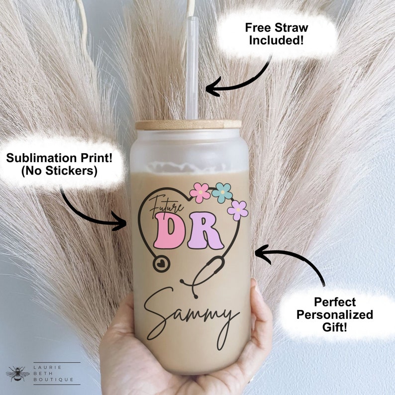 May include: A personalized tumbler with a brown background and a pink and blue heart with the text "Future DR" inside. The heart is surrounded by flowers. The name "Sammy" is written below the heart. The tumbler has a bamboo lid and comes with a free straw.