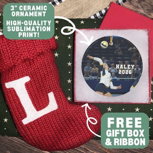 May include: A 3-inch round ceramic ornament featuring a sublimation print of a volleyball player in action, with the text HALEY 2026. The ornament is displayed alongside a red knit stocking with a white letter L and a red gift box.