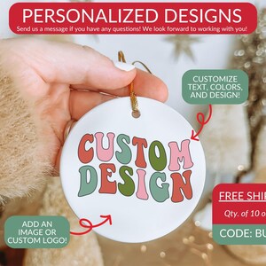 Op de afbeelding: Een rond wit keramieken ornament met de tekst CUSTOM DESIGN in een golvend, meerkleurig lettertype met tinten roze, rood en groen. Het ornament is voorzien van een gouden ophangkoord aan de bovenkant en wordt gepresenteerd als aanpasbaar product.