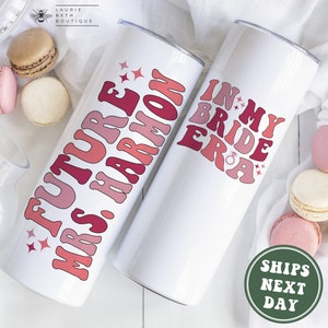 May include: Two white tumblers with pink and red text. The tumbler on the left says "Future Mrs. Harmon" and the tumbler on the right says "In My Bride Era".