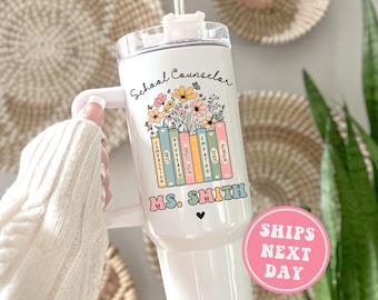 May include: White tumbler with a design of books and flowers. The text "School Counselor" and "MS. SMITH" are printed on the tumbler.