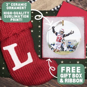 May include: A red knit Christmas stocking with a white letter "L" next to a 3-inch ceramic ornament with a lacrosse player image. The ornament is in a gift box with a red lid. The text says "3" ceramic ornament, high-quality sublimation print!" and "Free gift box & ribbon."