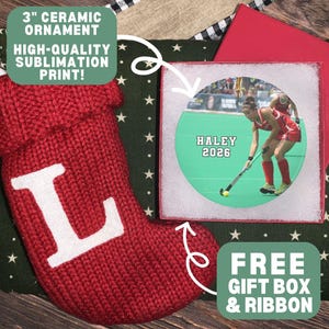May include: A 3-inch ceramic ornament featuring a sublimation print of a field hockey player with the text HALEY 2026, accompanied by a red knit stocking with a white letter L, a dark green star-patterned fabric, and a red gift box.