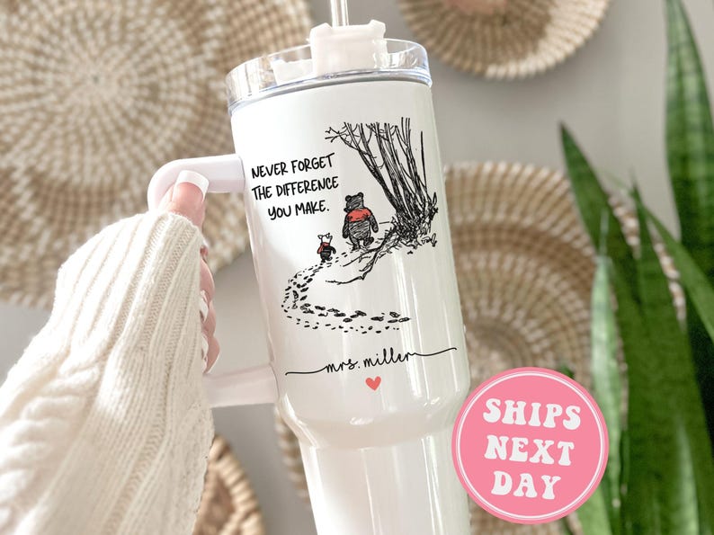 May include: White stainless steel tumbler with a black and white illustration of Winnie the Pooh and Piglet walking in the woods. The tumbler has a black lid and a black handle. The text "Never forget the difference you make." is printed on the tumbler. The text "mrs. miller" is printed on the tumbler below the illustration. A pink circle with the text "SHIPS NEXT DAY" is in the lower right corner of the image.