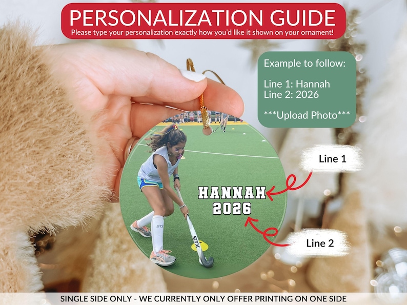 May include: A round, flat, custom photo ornament featuring a field hockey player on a green field. The text "HANNAH" and "2026" is printed in white with a black outline. A red arrow points to the name and another to the year for personalization.