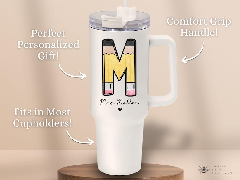 May include: White stainless steel travel mug with a black and yellow pencil design that spells out the letter "M". The mug has a black handle and a clear lid with a straw. The text "Mrs. Miller" is printed on the mug.