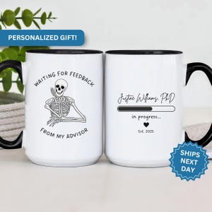 May include: Two white ceramic mugs with black handles. The mug on the left has a black and white illustration of a skeleton with the text "Waiting for feedback from my advisor". The mug on the right has the text "Justine Williams, PhD" with a progress bar and the text "in progress... Est. 2025".