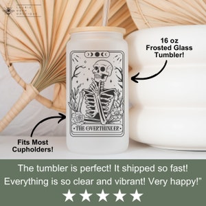 May include: A 16 ounce frosted glass tumbler with a black and white illustration of a skeleton with the text "The Overthinker" on a white background. The tumbler has a bamboo lid and a straw.