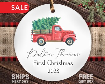 Könnte beinhalten: Ein weißer runder Weihnachtsbaumschmuck mit einem roten Lastwagen, der einen grünen Weihnachtsbaum transportiert. Der Schmuck ist mit dem Text "Dalton Thomas Erstes Weihnachten 2023" personalisiert.