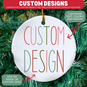May include: A round white ceramic ornament with a gold hanging string. The text CUSTOM DESIGN is printed in the center in a multi-colored sans-serif font using shades of red, pink, and sage green. The ornament features a small hole at the top.