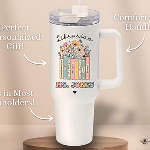 May include: White tumbler with a handle, featuring a floral design and the words "Librarian" and "MS. JONES". The tumbler is on a wooden surface.
