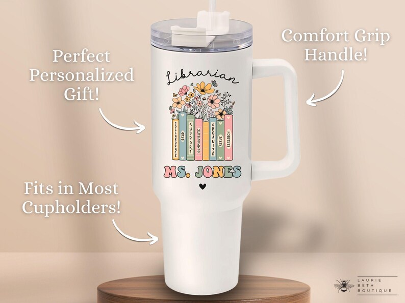 May include: White tumbler with a handle, featuring a floral design and the words "Librarian" and "MS. JONES". The tumbler is on a wooden surface.