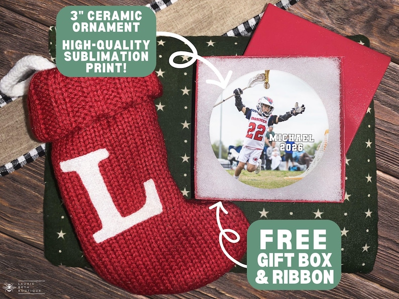 May include: A 3-inch round ceramic ornament featuring a sublimation print of a lacrosse player in a white uniform with the text MICHAEL 2026. The ornament is presented in a gift box alongside a red knitted Christmas stocking with a white letter L.