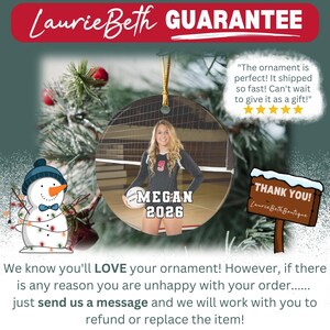 May include: A round ceramic ornament featuring a photograph of a volleyball player holding a ball, with the text MEGAN 2026 printed below. The ornament includes a gold hanging string and is displayed alongside a snowman graphic and a wooden sign.