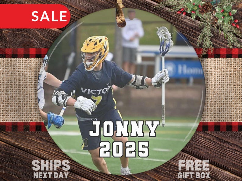 May include: Round ornament featuring a lacrosse player in a navy blue uniform with the word "VICTOR" and the number 7. The ornament has the name "JONNY 2025" in large white letters. The background shows a green field.