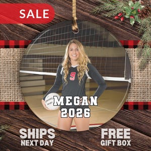 May include: A round ceramic ornament featuring a photograph of a volleyball player in a black jersey with the number 9, holding a white volleyball. The text MEGAN and 2026 is printed in white block letters over the center of the image.