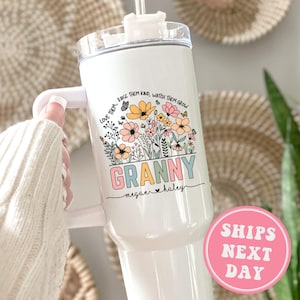 May include: White tumbler with a floral design and the text "LOVE THEM. RAISE THEM KIND, WATCH THEM GROW GRANNY megan haley".