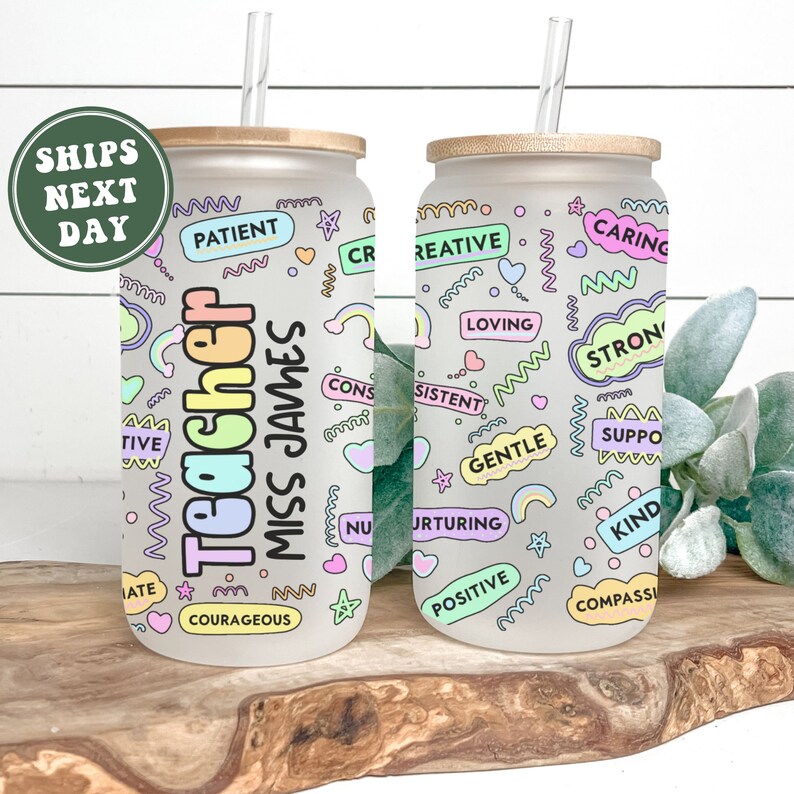 Puede incluir: Dos vasos de vidrio esmerilado con tapas de bamb&uacute; y pajitas. Los vasos est&aacute;n decorados con palabras y dise&ntilde;os coloridos, incluyendo "Teacher" y "Miss James".