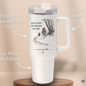 May include: White travel mug with a black and white illustration of Winnie the Pooh and Piglet walking in the woods. The mug has a black handle and a black lid with a straw. The text "Never forget the difference you make." is printed on the mug. The mug is personalized with the name "mrs. smith".