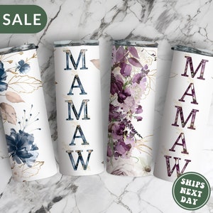 May include: Four stainless steel tumblers with different floral designs. The tumblers are white with gold accents and feature the word "MAMAW" in black lettering.