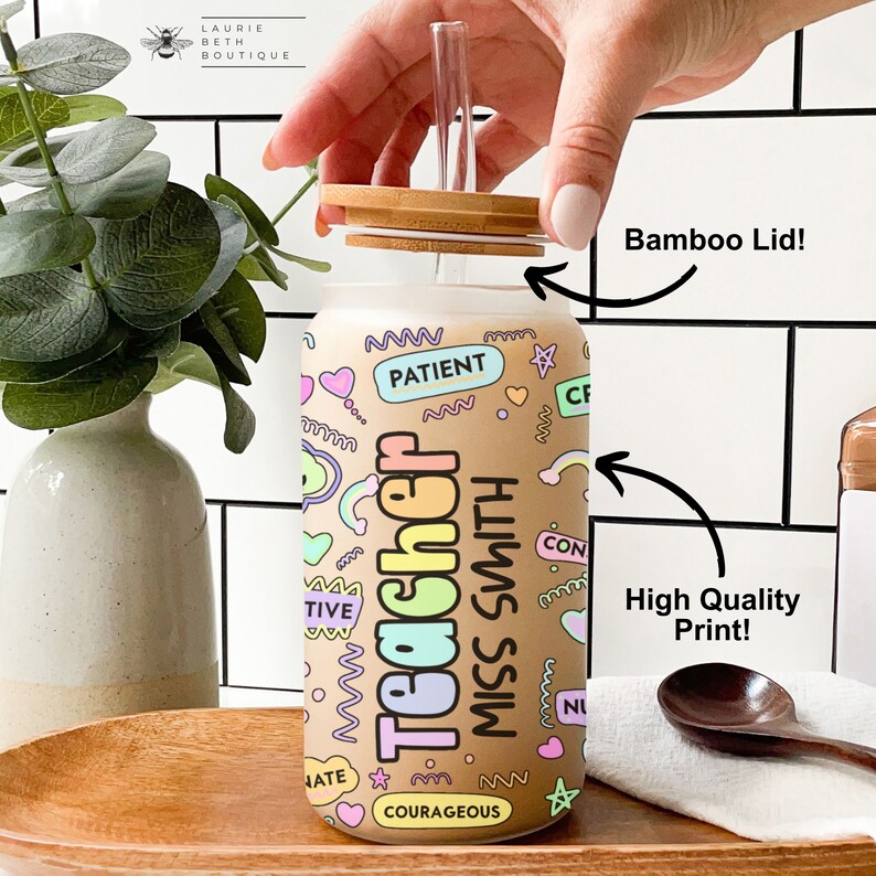 Puede incluir: Una botella de agua reutilizable de vidrio transparente con tapa de bamb&uacute; y una pajita. La botella tiene un dise&ntilde;o colorido con las palabras "Teacher Miss Smith" y otras palabras positivas como "paciente", "creativo" y "valiente".