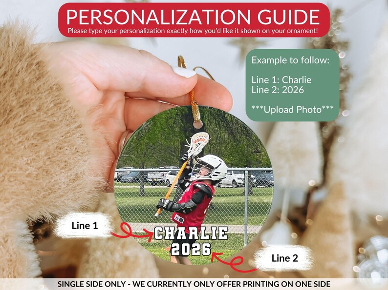 May include: A round, personalized ornament featuring a photograph of a lacrosse player in a red jersey and white helmet holding a lacrosse stick. The text 'CHARLIE' appears on line one and '2026' on line two in white block letters with black outlines.