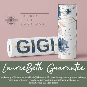 May include: Two stainless steel tumblers with a floral design in shades of blue and gold. The tumblers are personalized with the name "GIGI" and the names "Megan" and "Samantha" in a smaller font. The tumblers are on a pink background with the text "Laurie Beth Boutique" above them.