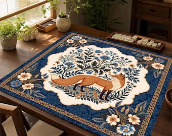 Puede incluir: Una alfombrilla de tela cuadrada con una ilustración central de un zorro rojo de pie entre patrones florales azules y blancos. El diseño se presenta sobre un fondo azul profundo con un borde decorativo, mostrando un motivo botánico.