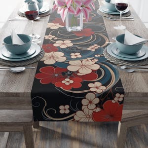 Könnte beinhalten: Ein schwarzer Tischläufer mit einem Blumendesign mit roten, weißen und blauen Blumen. Die Blumen sind stilisiert und haben einen japanisch inspirierten Look. Der Läufer liegt auf einem Holztisch mit zwei Gedecken auf jeder Seite.