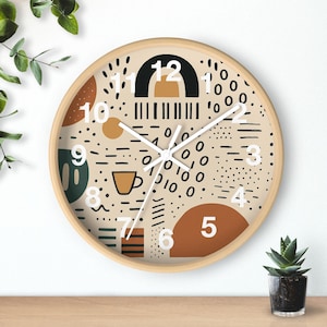 May include: A round wall clock with a light wood frame. The clock face features a beige background with abstract shapes in black, brown, and orange. White hands indicate the time. Numbers are in white.
