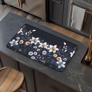May include: A dark blue kitchen mat with a white floral design. The flowers are arranged in a row along the bottom edge of the mat. The flowers are white with yellow centres and have a delicate, realistic look.