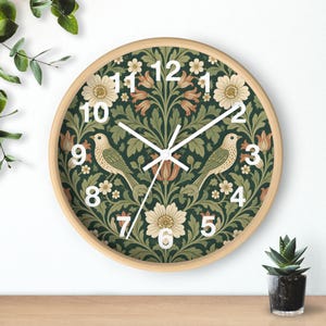 May include: A round wall clock with a light wood frame featuring a dark green background with a repeating pattern of cream-coloured flowers, green leaves, and two birds. The clock face has white numbers from 1 to 12 and white clock hands.