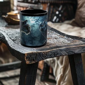 May include: Black ceramic mug with a graphic of an owl and a cat in a forest setting under a full moon.