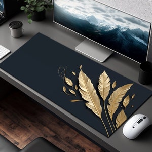May include: A dark blue desk mat with a design of gold feathers. The mat is on a wooden desk with a computer monitor, a mouse, and a plant.