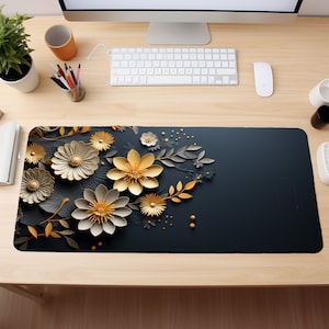 May include: A black desk mat with a floral design featuring gold and white paper flowers. The flowers are arranged in a cluster on the left side of the mat, with the rest of the mat being a solid black color.