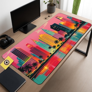 Può includere: Un vivace tappetino per scrivania con un design colorato di paesaggio urbano e palme. L'opera d'arte presenta edifici nei toni del giallo, arancione, rosso e verde acqua su un cielo rosa. Il tappetino rettangolare è appoggiato su una scrivania di legno.