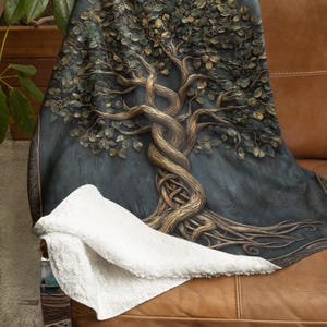 Puede incluir: Una manta de tiro con un fondo azul oscuro que presenta un diseño dorado de árbol de la vida con detalles intrincados. El árbol tiene un patrón de nudo celta y está rodeado por un borde dorado.