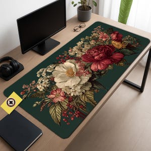 May include: A rectangular desk mat featuring a dark green background with a large floral design. The floral arrangement includes a large white flower, a deep red peony, and various smaller flowers in shades of pink, cream, and yellow. The mat is designed to protect the desk surface.