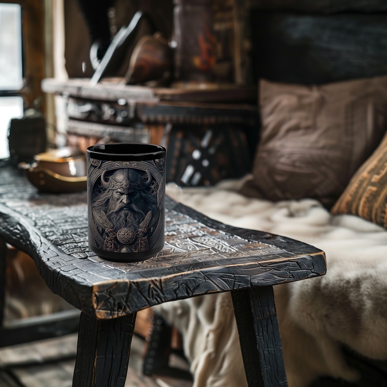 May include: A black ceramic mug with a detailed image of a Viking warrior with a beard and horned helmet. The mug is sitting on a wooden table.