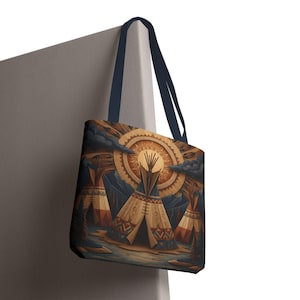 May include: Tote bag featuring a detailed illustration of Native American teepees, a sunburst design, and mountain scenery. The bag has a navy blue handle and a colorful, artistic design.