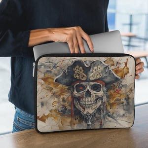 May include: A laptop sleeve with a watercolor design of a skull wearing a pirate hat. The skull has one red eye and a gold and red bandana. The background is a mix of brown, yellow, and white.