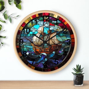 Könnte beinhalten: Eine runde Uhr mit einem Buntglasdesign, das ein Schiff zeigt, das auf einem blauen und grünen Meer segelt. Das Zifferblatt der Uhr hat römische Ziffern und einen schwarzen Zeiger. Die Uhr ist in einem hellbraunen Holzrahmen gefasst.