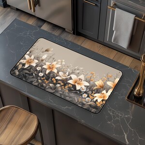 May include: A beige kitchen mat with a floral design featuring white lilies and green leaves. The mat has a subtle sheen and a textured surface.
