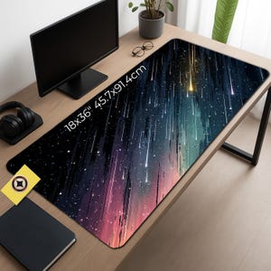Op de afbeelding: Een rechthoekige bureaumat met een kosmisch ontwerp, met een donkere achtergrond met strepen van wit en geel licht. De mat meet 45,7 cm x 91,4 cm en is geplaatst op een houten bureau. De tekst "18x36" 45.7x91.4cm" is op de mat gedrukt.