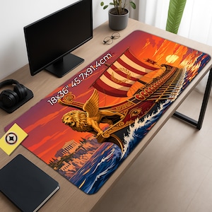 Op de afbeelding: Een rechthoekige bureaumat met een levendige illustratie van een antiek galei met een gevleugelde leeuw als boegbeeld, varend bij zonsondergang. De mat toont de tekst 18x36" 45.7x91.4cm en een kuststad met een tempel op de achtergrond.